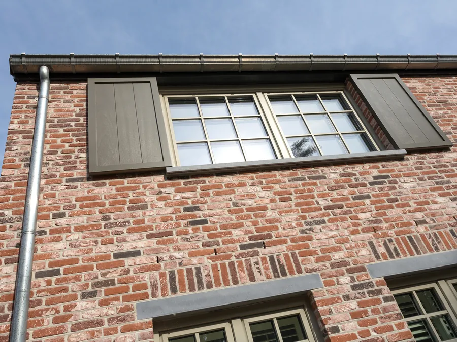Façade en brique avec fenêtre à petits bois encadrée de volets battants gris