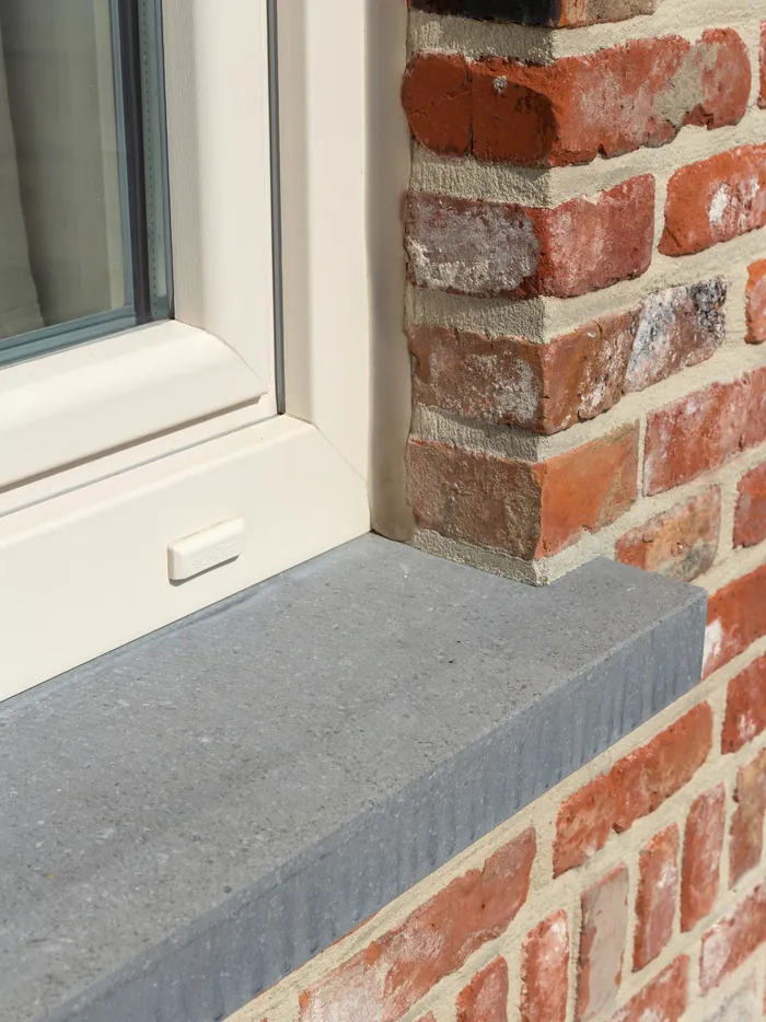 Détail d'une fenêtre crème posée sur un appui en pierre bleue, brique rouge