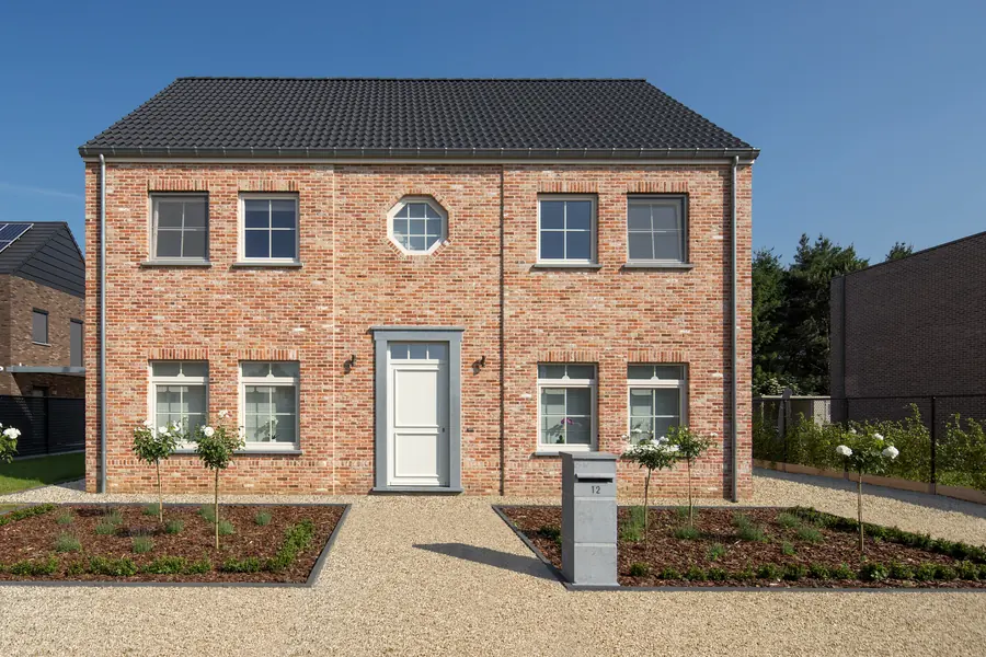 Maison en brique symétrique, fenêtres blanches à petits bois, oculus et porte blanche
