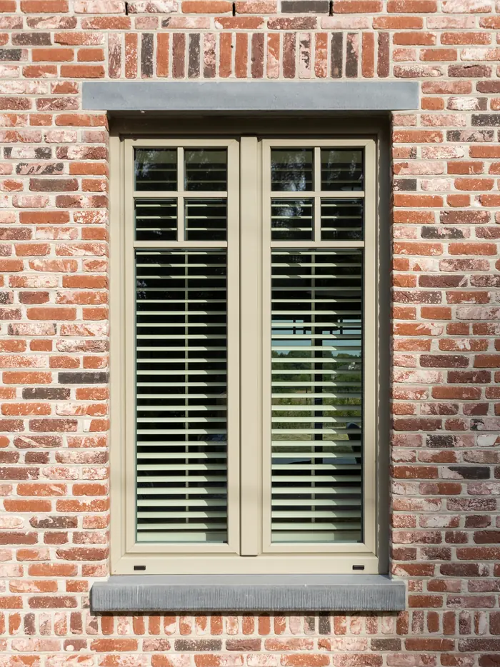 Haute fenêtre à petits bois avec stores intérieurs dans une façade en brique