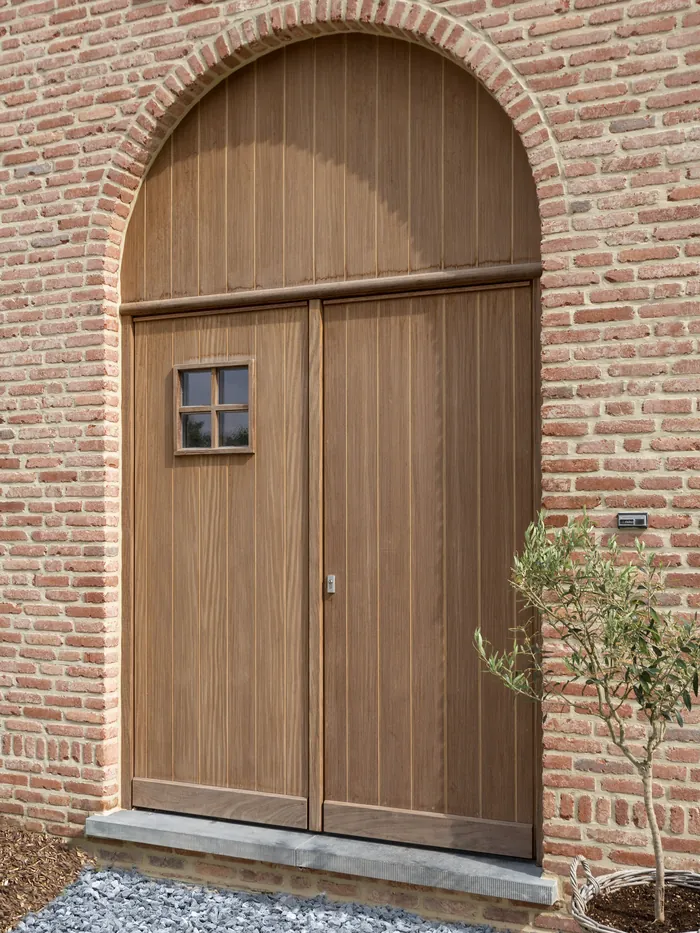 Porte d'entrée cintrée en chêne à deux vantaux dans un mur de brique
