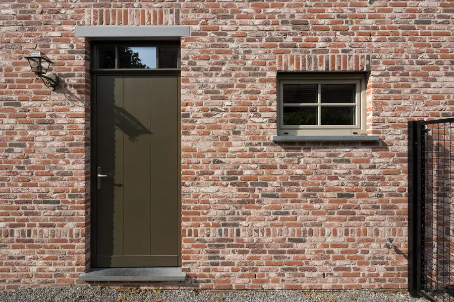 Porte pleine brun foncé et petite fenêtre dans un mur de brique